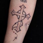 Tatouage de croix et chapelet en noir sur le bras